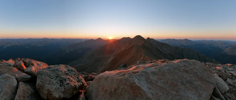 Panoramic view from rocky mountain ridge at sunrise with jagged peaks and valley below