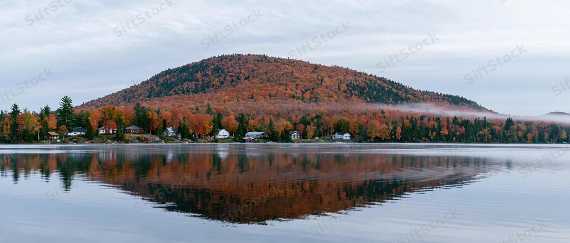 Calm lake reflecting autumn foliage on a forested mountain and shoreline homes