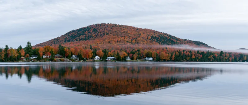 Panoramic view of a calm lake reflecting autumn foliage cover