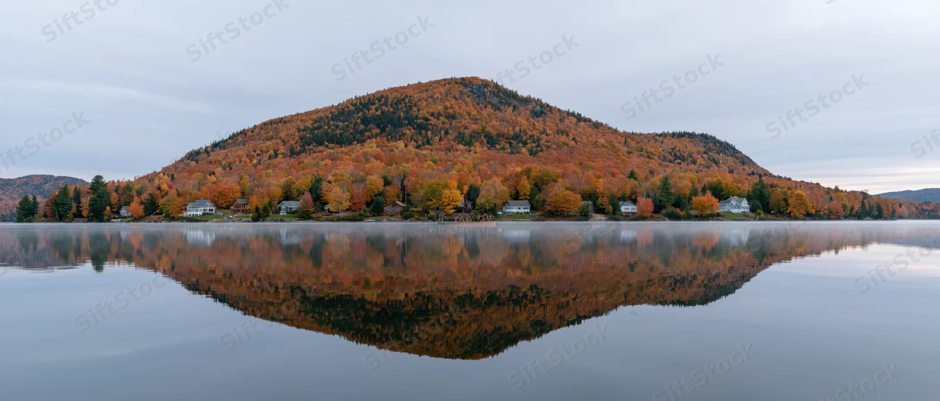 Calm lake reflecting autumn foliage-covered mountain and shoreline homes