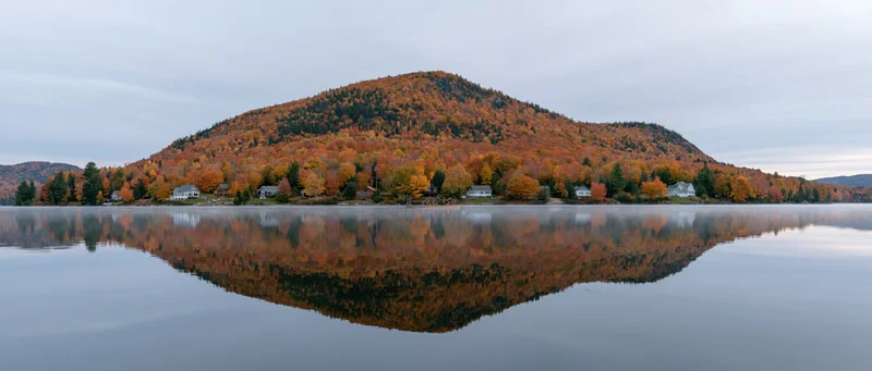 Panoramic view of a lake reflecting autumn foliage cover