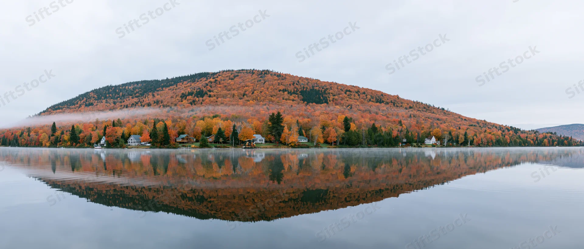 Calm lake reflecting autumn foliage and forested hillside with homes along the shore