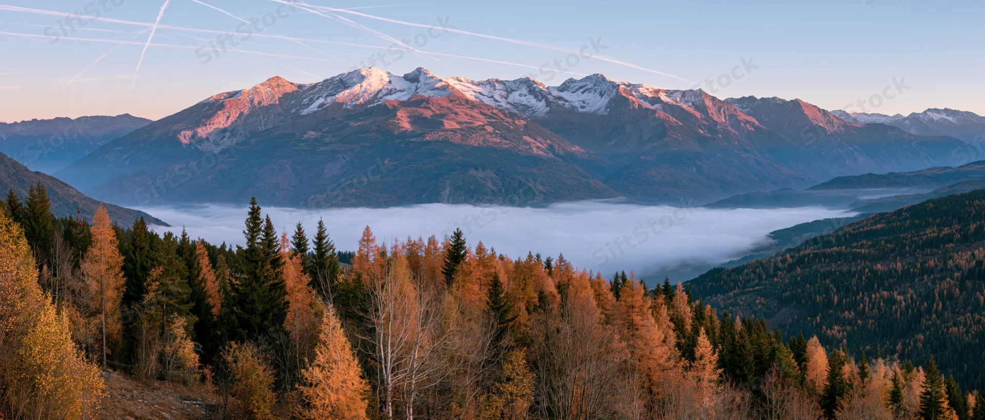 Snow-capped mountain range rising above fog-filled valley with autumn forest in foreground
