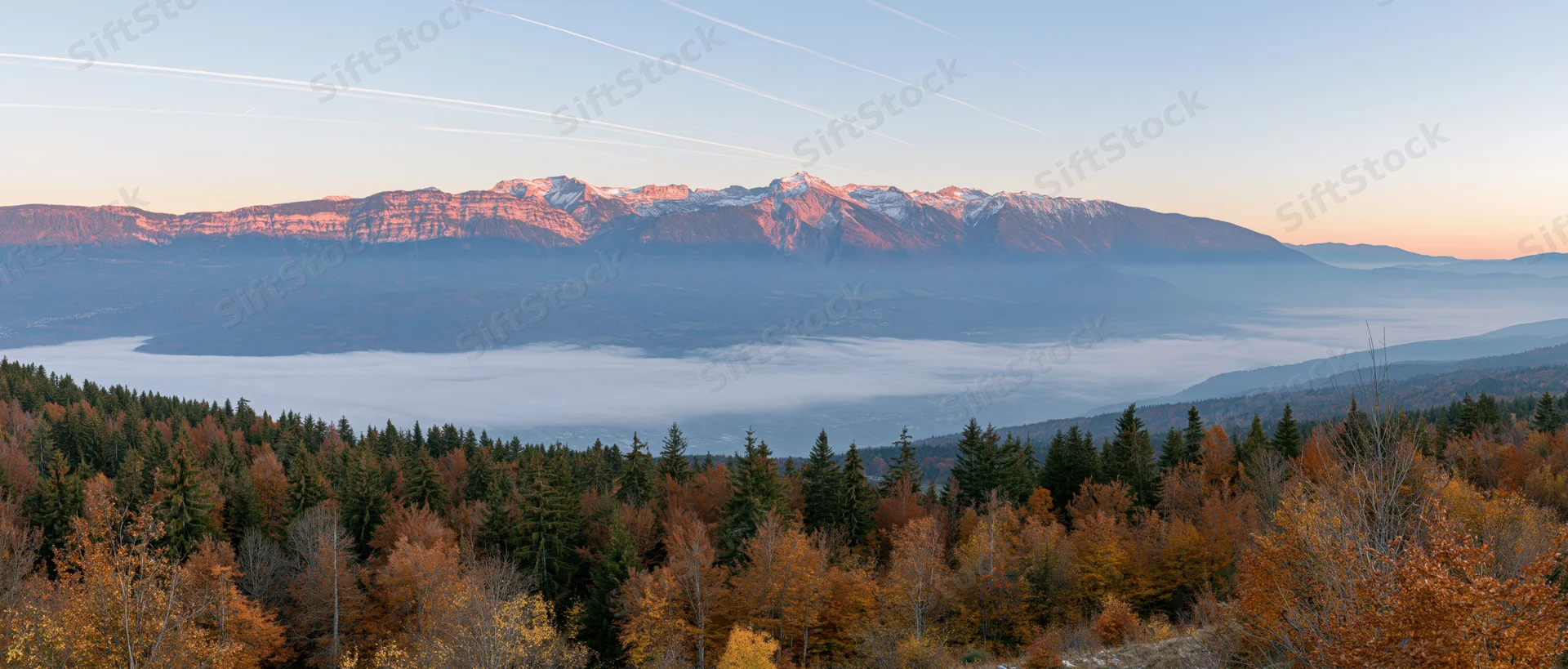 Snow-capped mountain range rising above misty valley with autumn forest in foreground