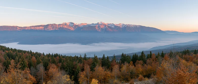 Snow-capped mountain range rising above misty valley with autumn forest in foreground