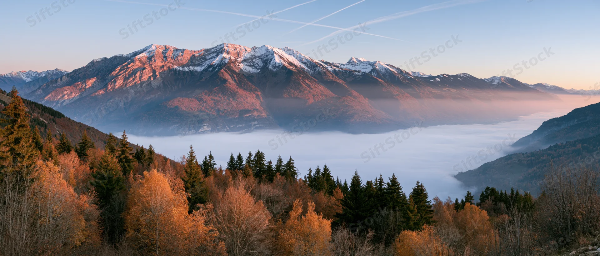 Snow-capped mountain range rising above fog-filled valley with autumn forest in foreground