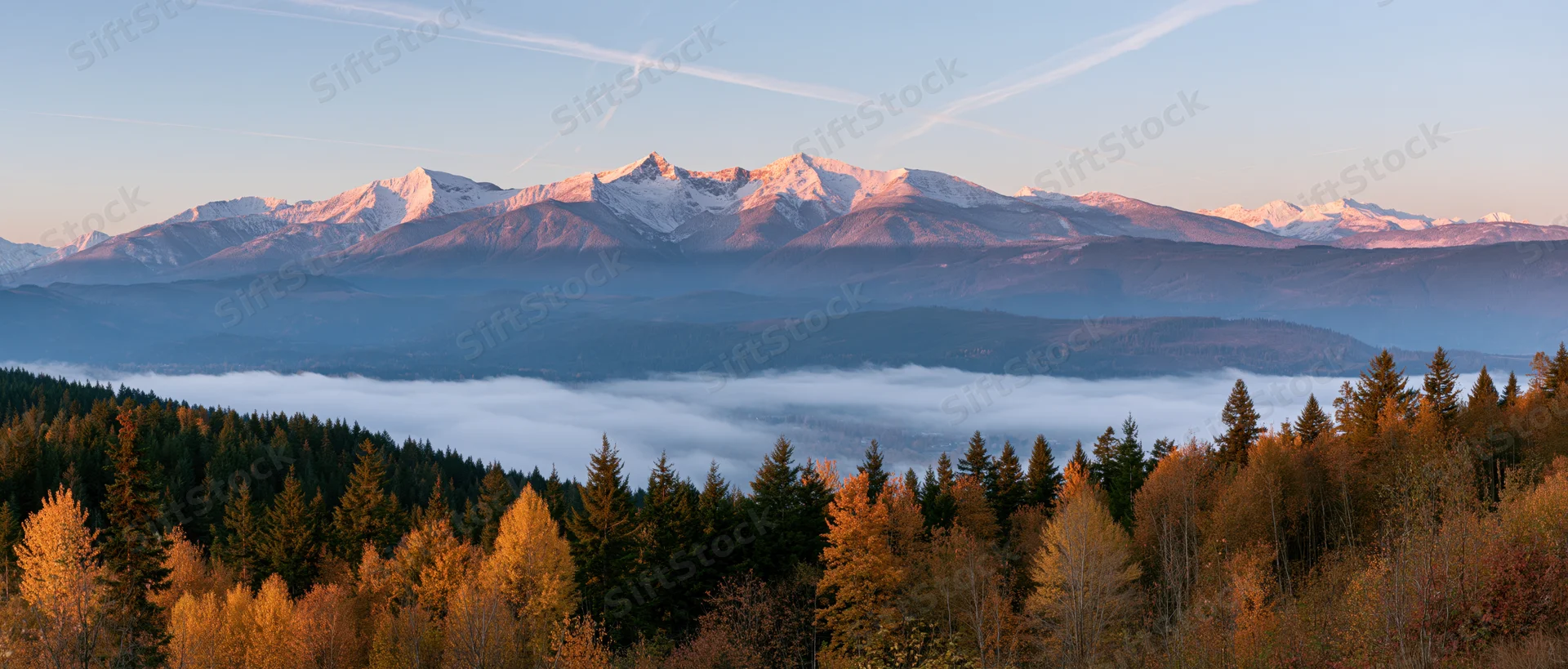 Snow-capped mountains rising above a misty valley with autumn forest in foreground