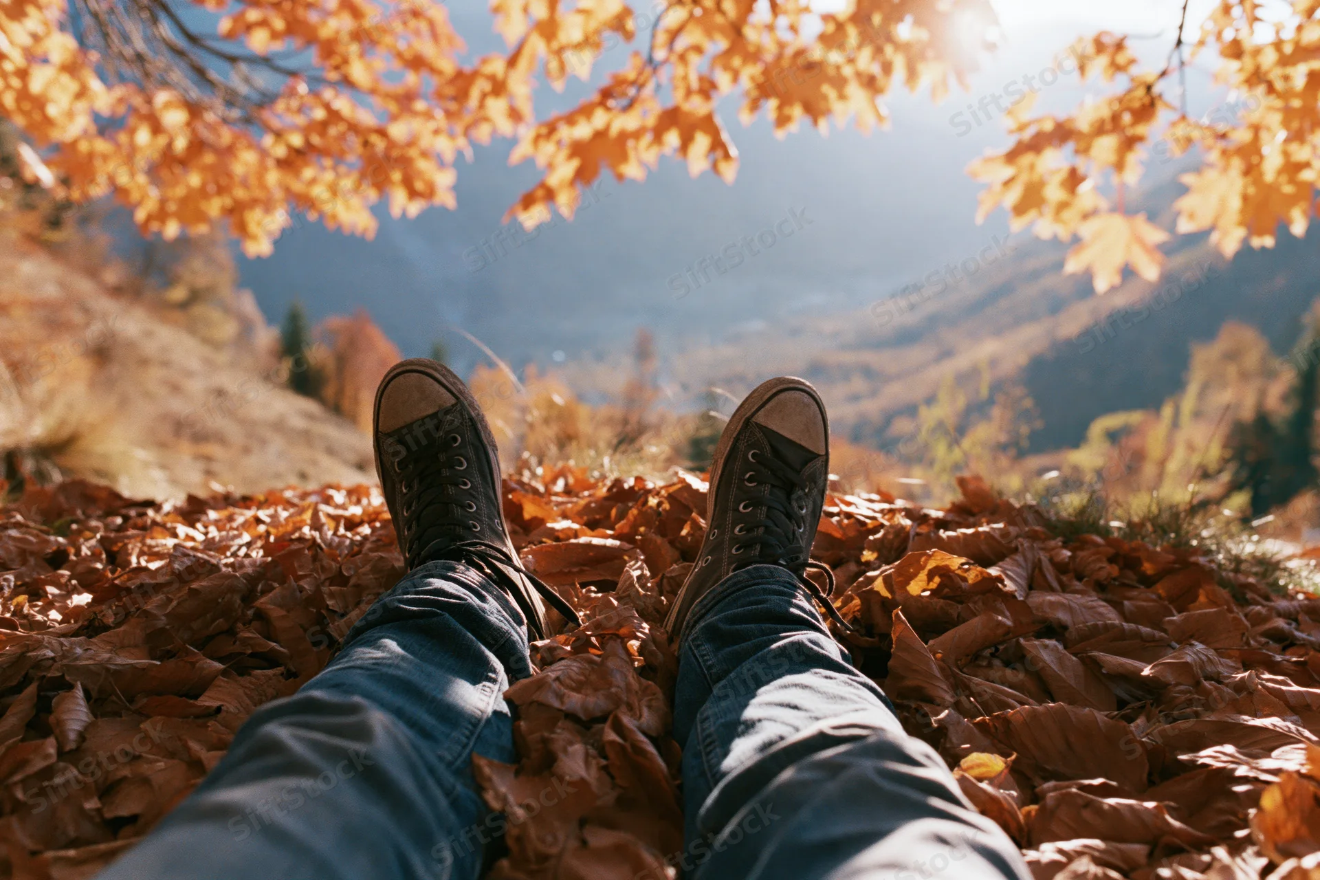 Legs in jeans and sneakers resting on a carpet of fallen autumn leaves overlooking a mountain valley