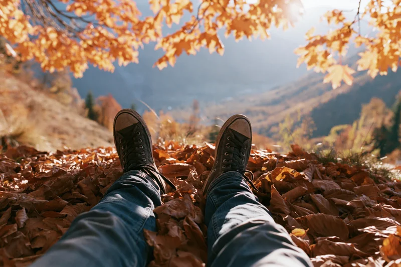 Legs in jeans and sneakers resting on a carpet of fallen autumn leaves overlooking a mountain valley
