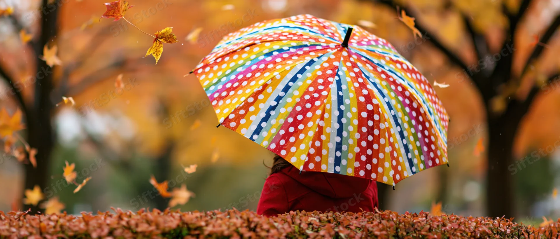 Woman holding colorful polka dot umbrella in autumn park with falling leaves