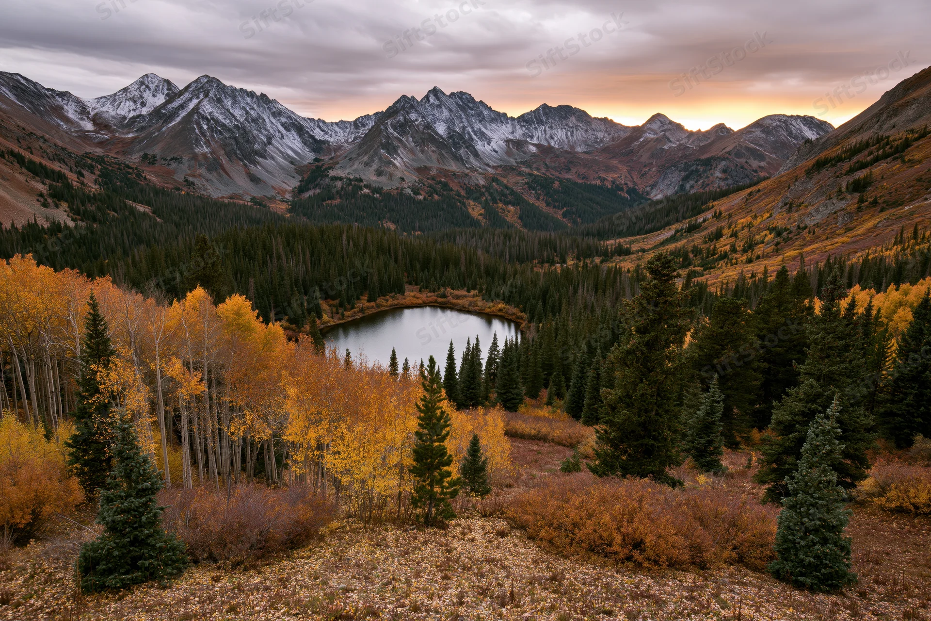 Alpine lake surrounded by autumn-colored aspen and evergreen trees in a mountain valley at sunset