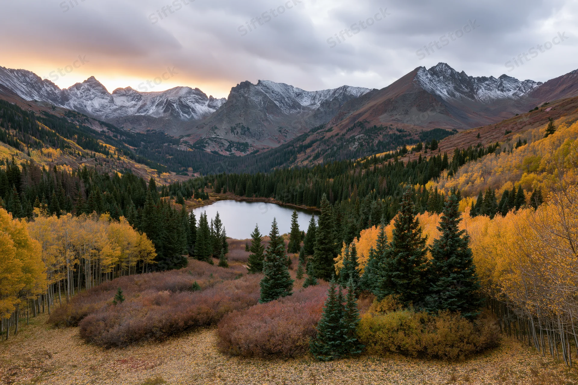 Alpine lake surrounded by golden aspen and evergreen trees in a mountain valley at autumn sunset