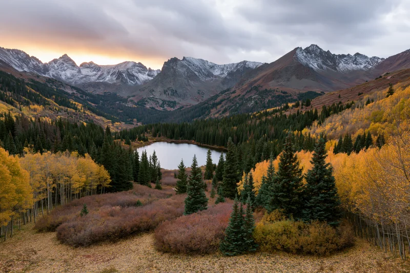 Alpine lake surrounded by golden aspen and evergreen trees in a mountain valley at autumn sunset