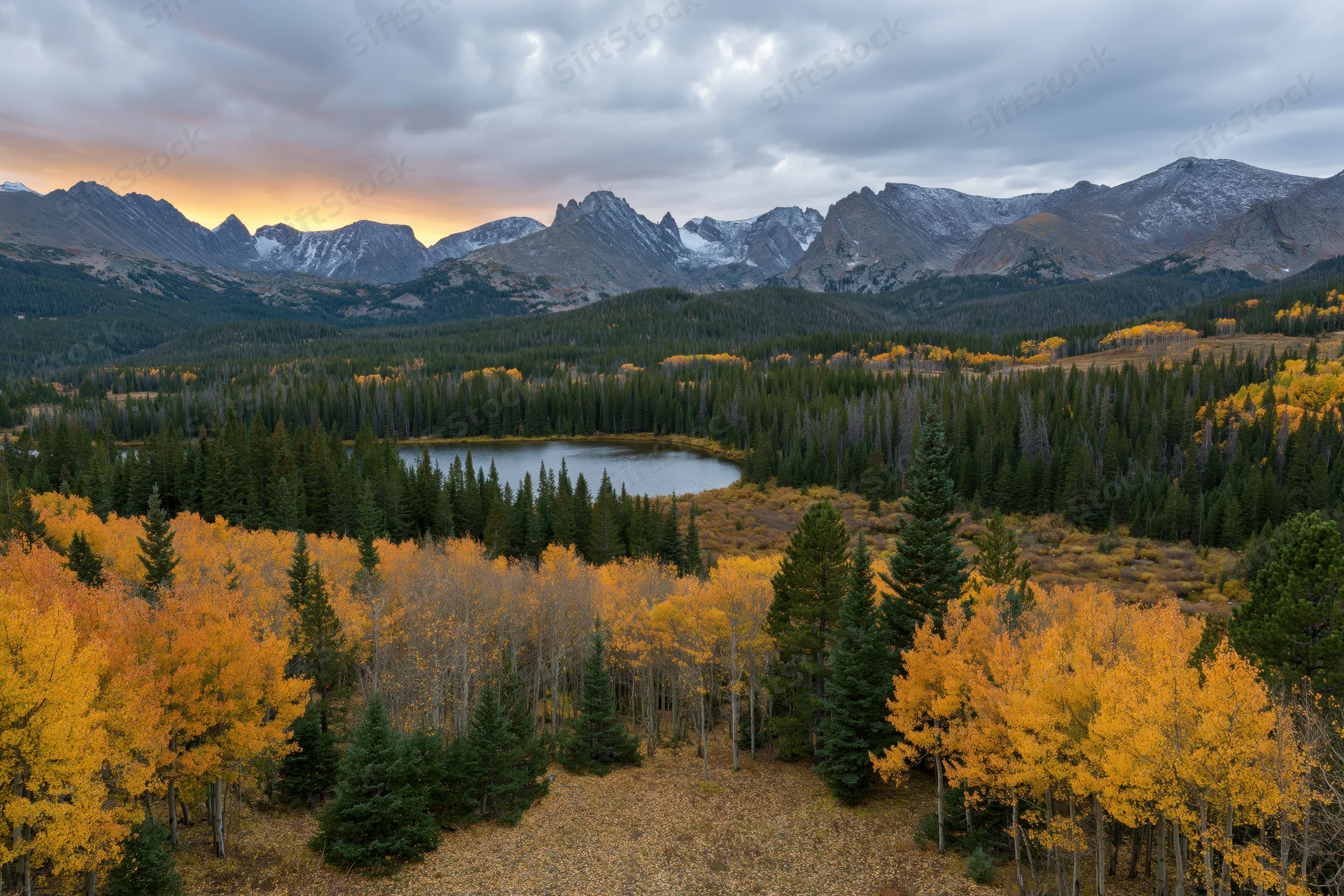 Autumn landscape with golden aspen trees and a small alpine lake surrounded by snow-capped mountains and evergreen forest