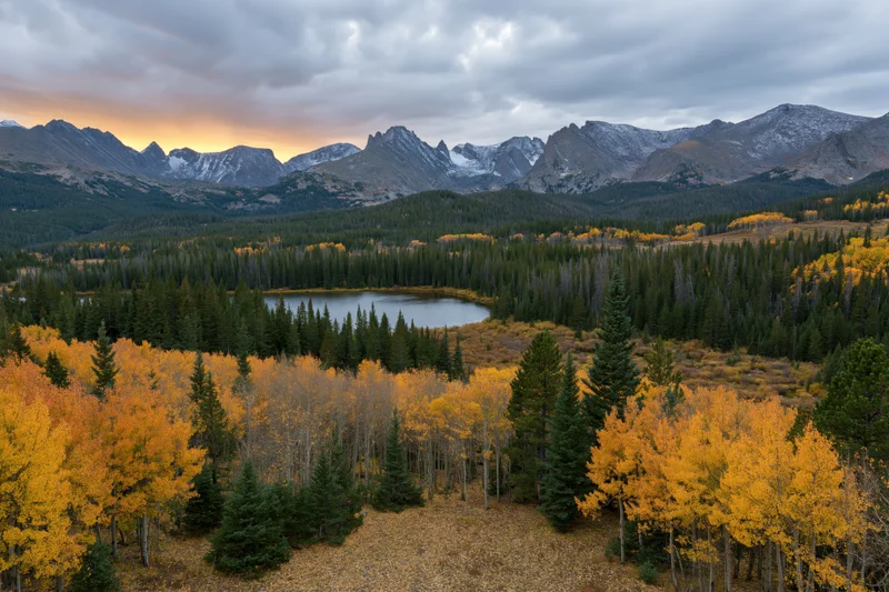 Autumn landscape with golden aspen trees and a small alpine lake surrounded by snow-capped mountains and evergreen forest