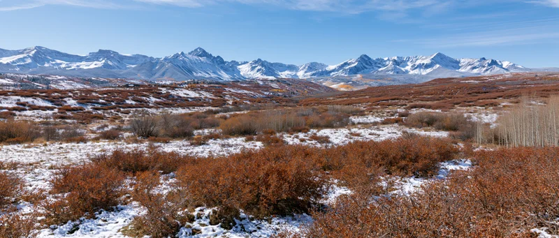Snow-dusted foothills with autumn shrubs under rocky mountain peaks in a wide valley