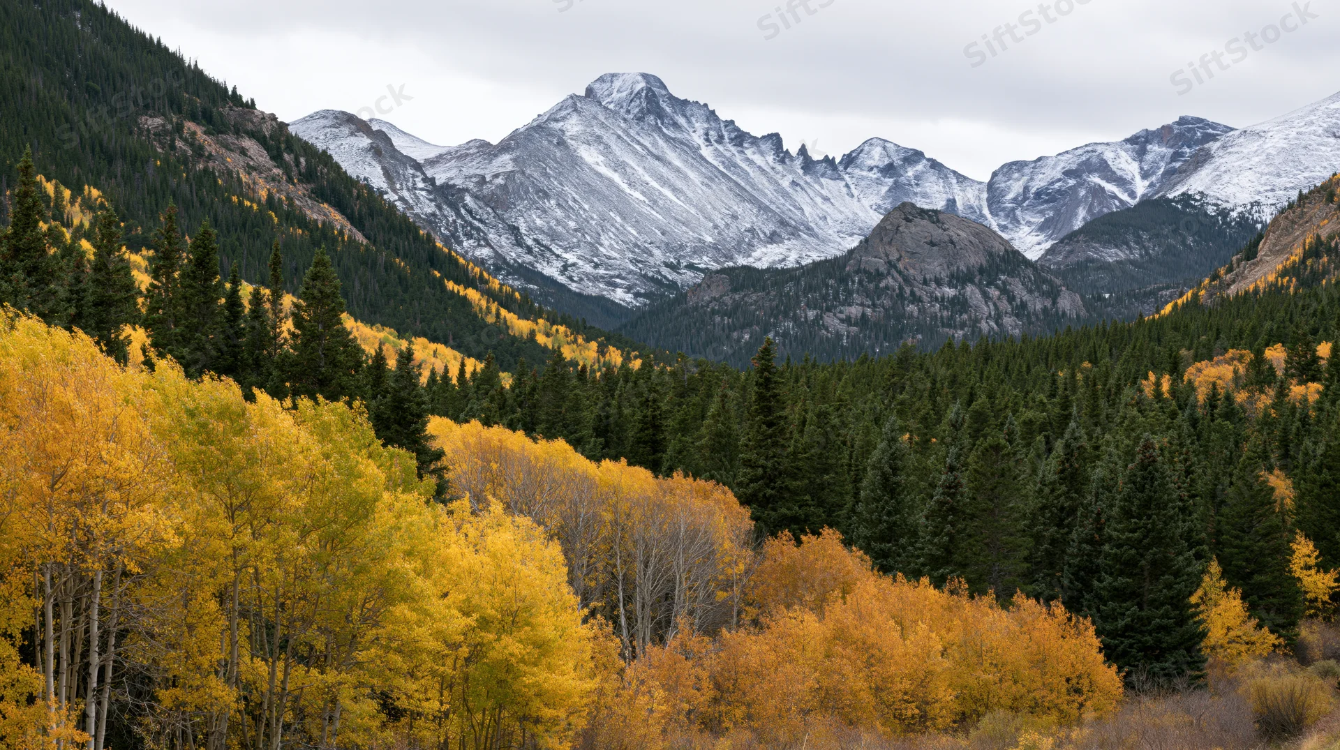 Snow-capped mountain peak rising above autumn forest in alpine valley