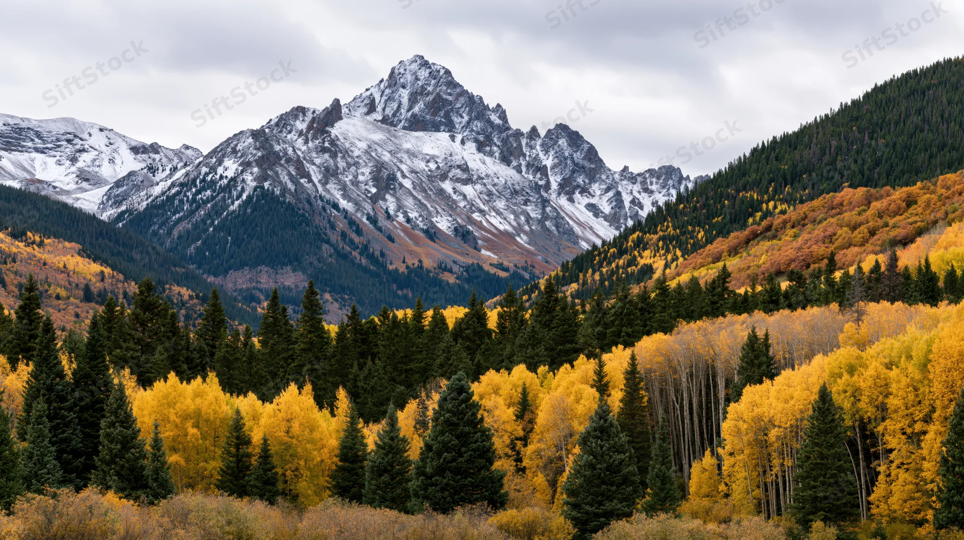 Snow-dusted rocky mountain peak rising above autumn-colored aspen and evergreen forest in valley