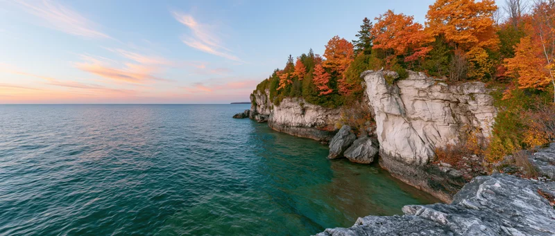 Rocky limestone cliff along a turquoise freshwater lake with autumn trees at sunset