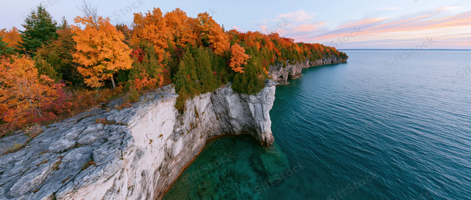 Rocky limestone cliff with autumn foliage overlooking turquoise freshwater lake at sunset