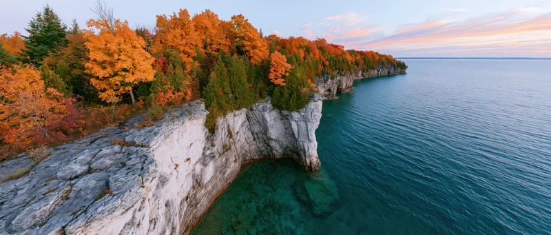 Rocky limestone cliff with autumn foliage overlooking turquoise freshwater lake at sunset
