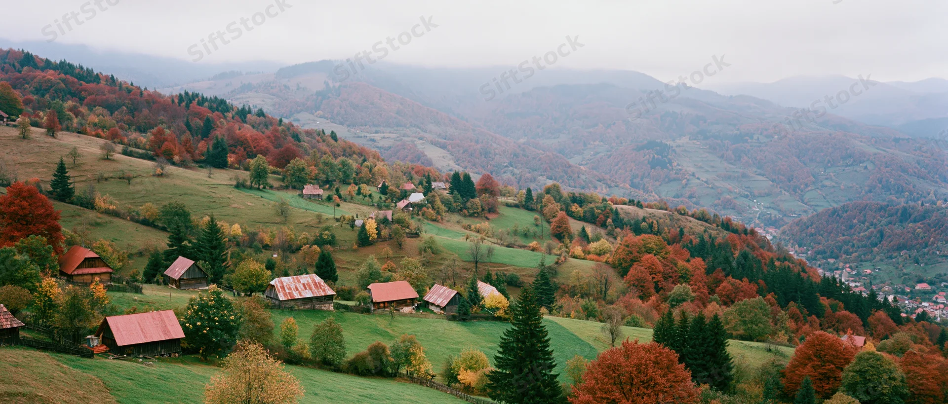 Rolling Carpathian hills covered in autumn foliage with scattered wooden cabins and green meadows under an overcast sky