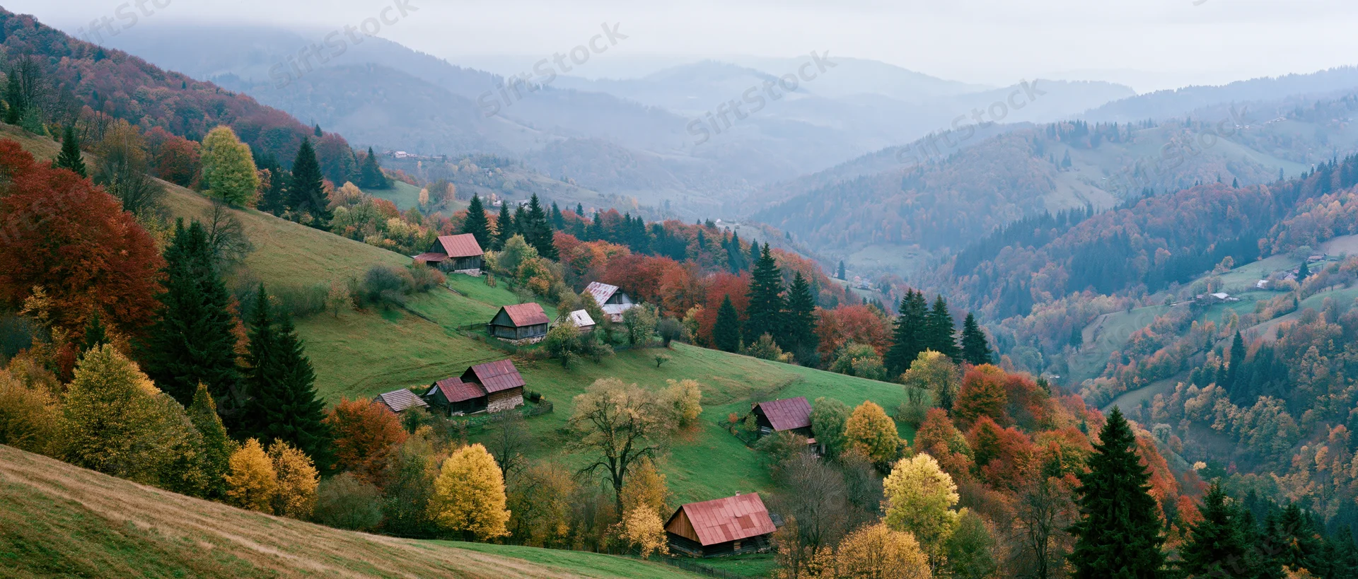 Rolling hills covered in autumn foliage with scattered wooden cabins in a mountain valley