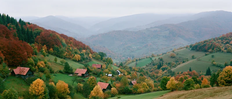 Rolling hills covered in autumn foliage with scattered wooden cabins in a mountain valley