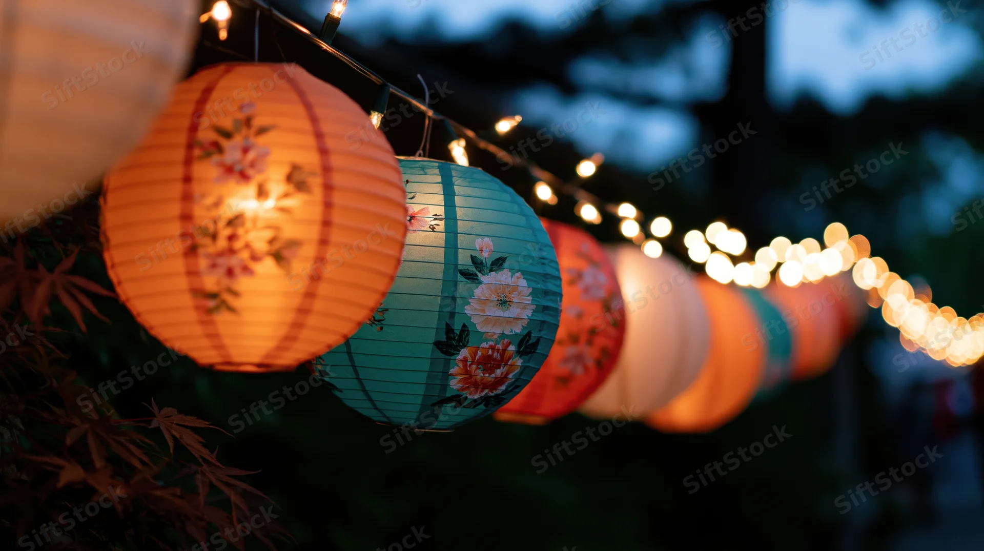 Glowing chinese paper lanterns with floral patterns hanging in a garden at twilight