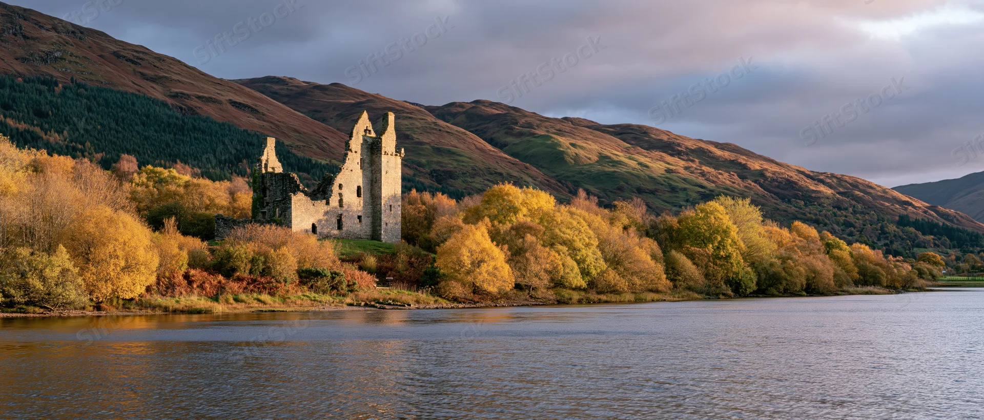 Medieval castle ruins beside a lake surrounded by autumn trees and mountains