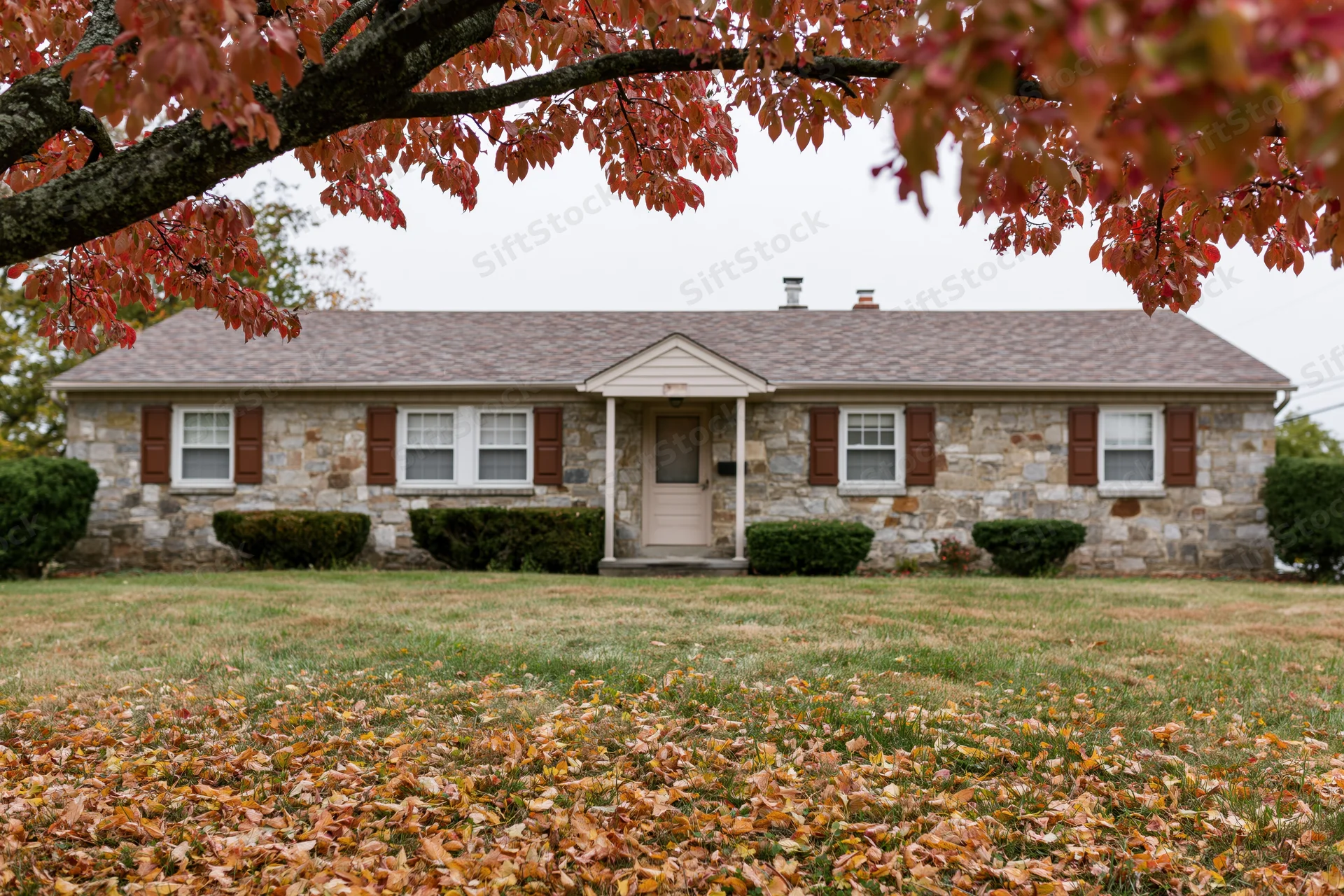 Stone ranch house with brown shutters and autumn leaves on lawn