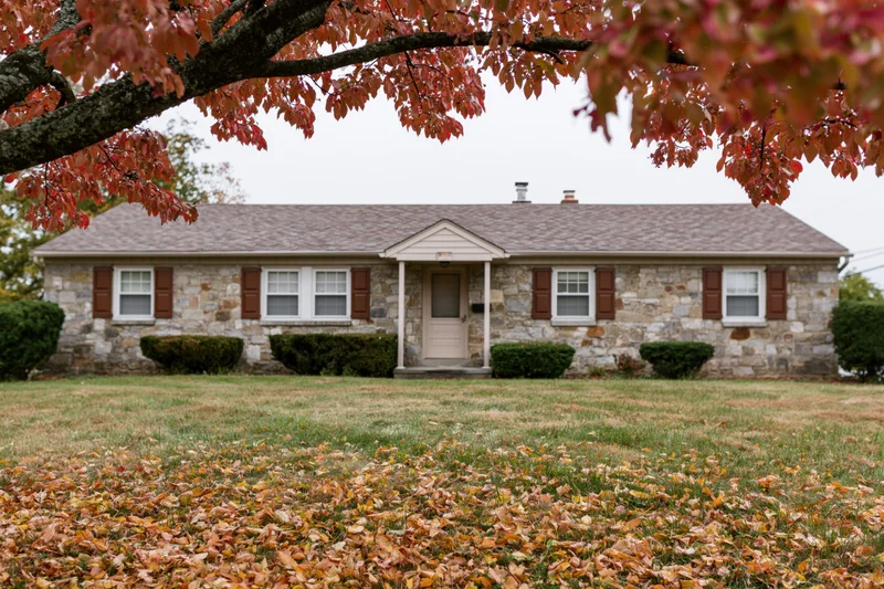 Stone ranch house with brown shutters and autumn leaves on lawn