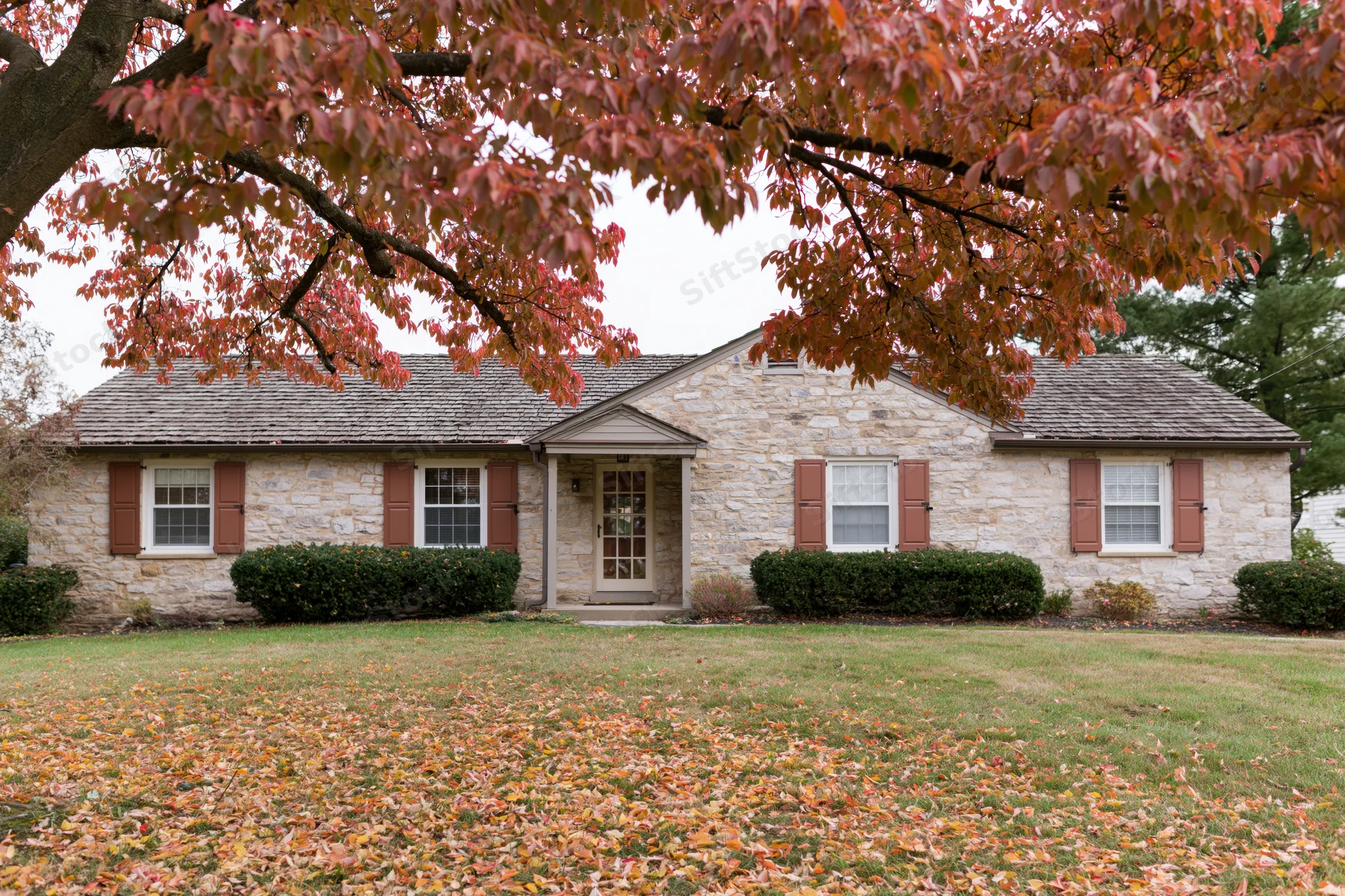 Stone ranch house with brown shutters and autumn leaves on lawn