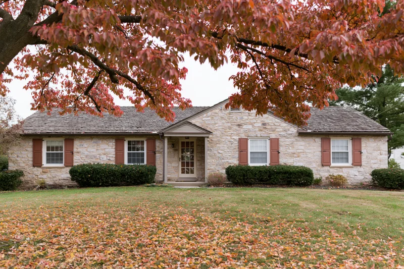 Stone ranch house with brown shutters and autumn leaves on lawn