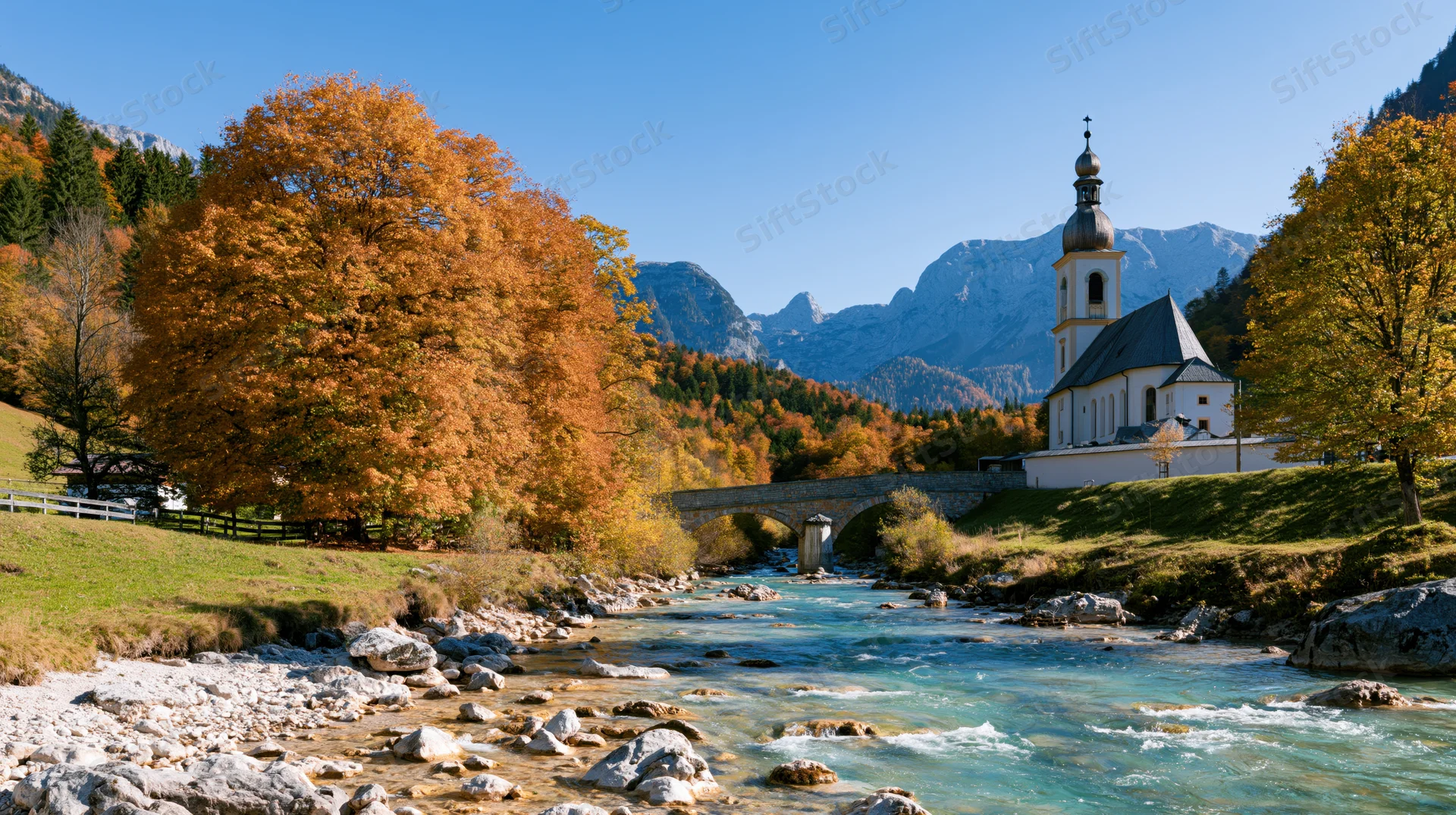 White church with onion dome steeple beside a flowing river in a mountain valley surrounded by autumn trees