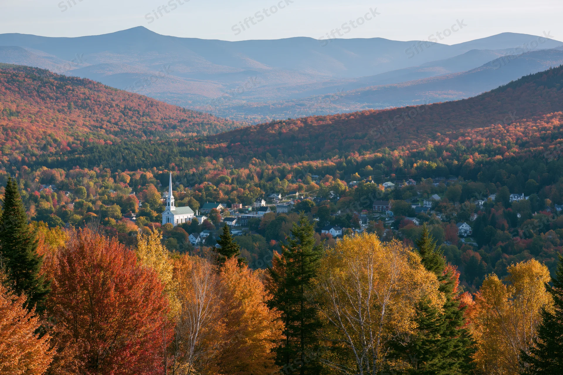 Small new england village nestled in a valley surrounded by autumn foliage and mountains viewed from an overlook
