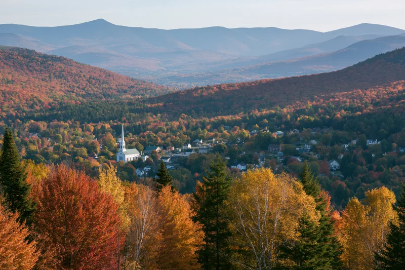 Small new england village nestled in a valley surrounded by autumn foliage and mountains viewed from an overlook