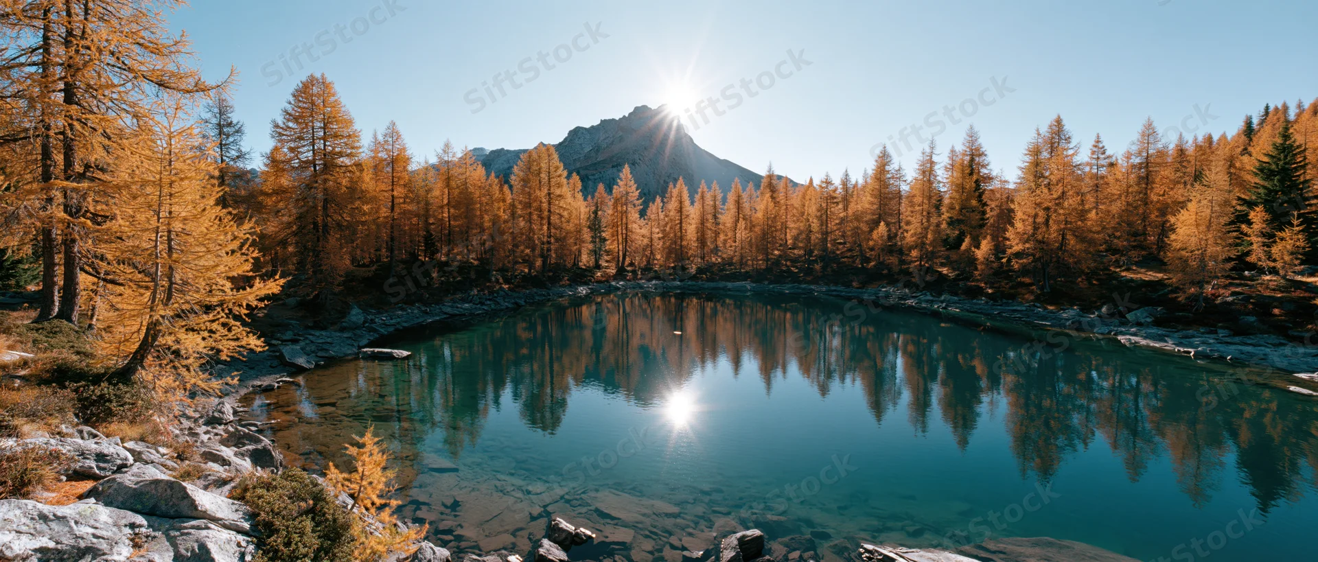 Alpine lake reflecting golden autumn trees and mountain under bright sun