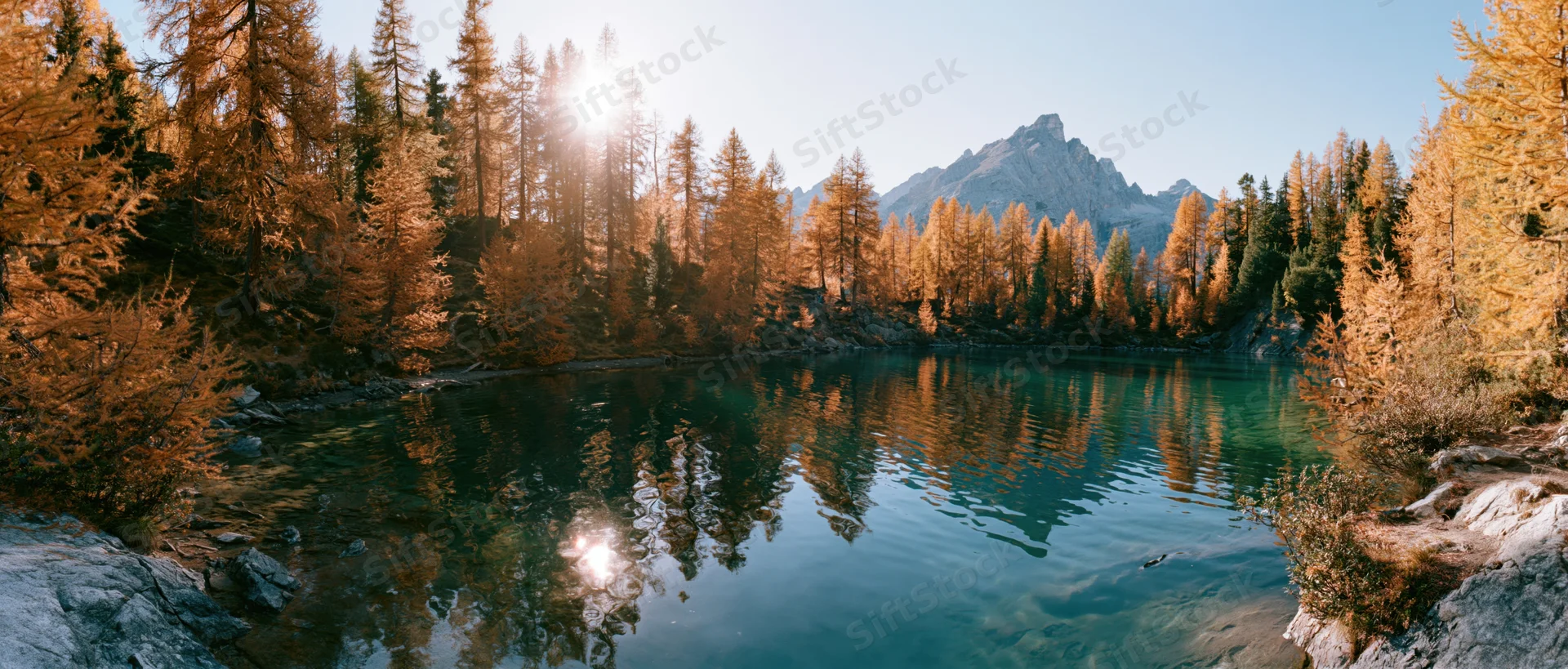 Alpine lake reflecting golden trees and mountains at sunrise