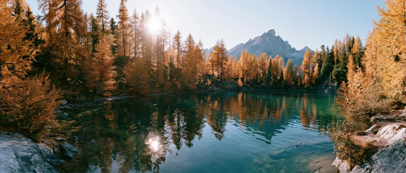 Alpine lake reflecting golden trees and mountains at sunrise