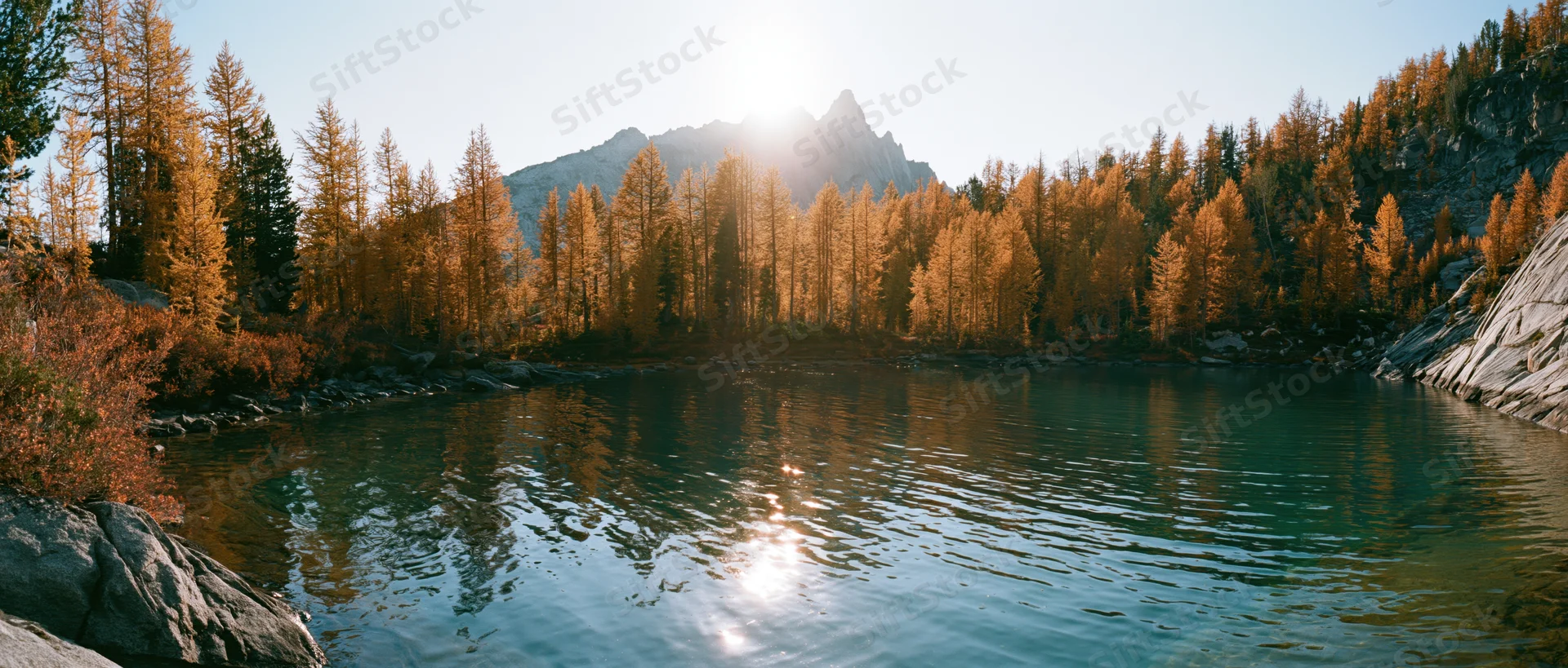 Alpine lake with clear turquoise water reflecting golden autumn trees and mountain peak at sunrise