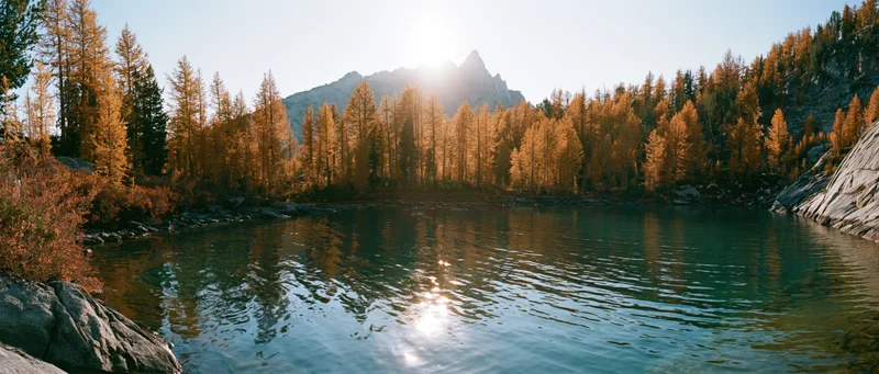 Alpine lake with clear turquoise water reflecting golden autumn trees and mountain peak at sunrise