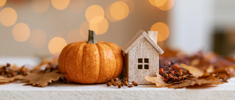 Small orange pumpkin and wooden house figurine arranged with autumn leaves and berries on a table