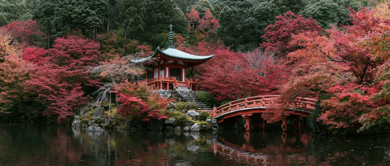 Small red japanese pagoda with green copper roof nestled among vibrant red maple trees beside a calm pond with a wooden bridge and reflections