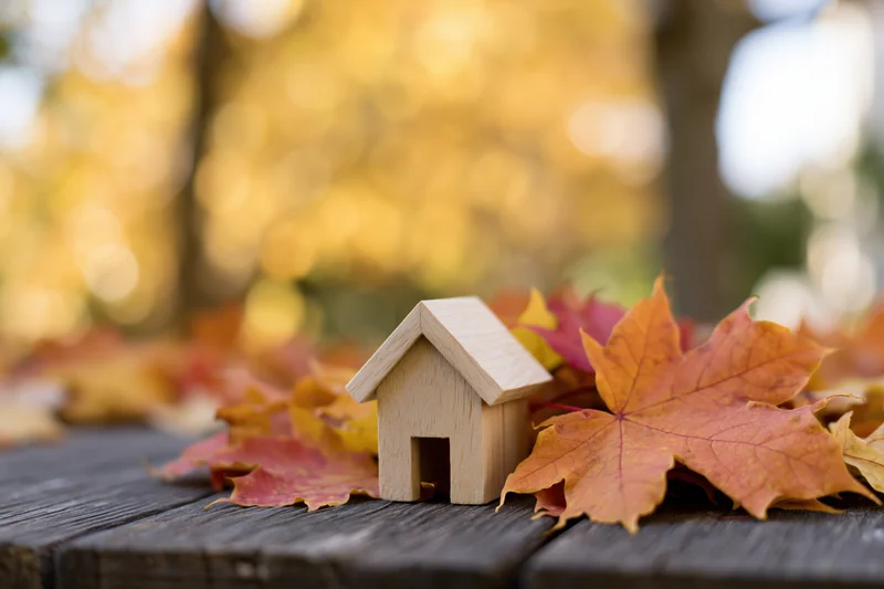 Small wooden house figurine resting on dark weathered wood among autumn maple leaves