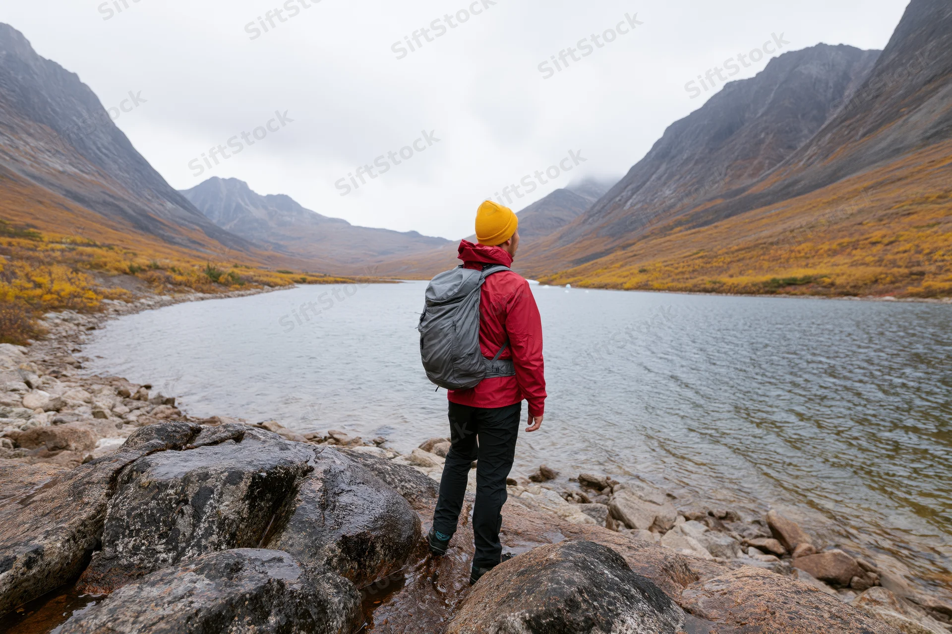 Solo hiker standing on rocky lakeshore looking toward mountains in autumn landscape