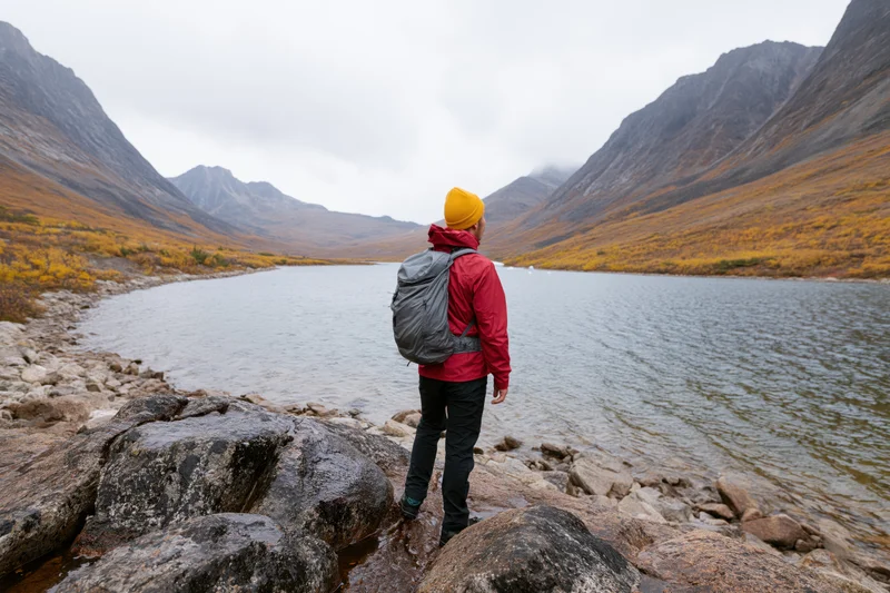 Solo hiker standing on rocky lakeshore looking toward mountains in autumn landscape