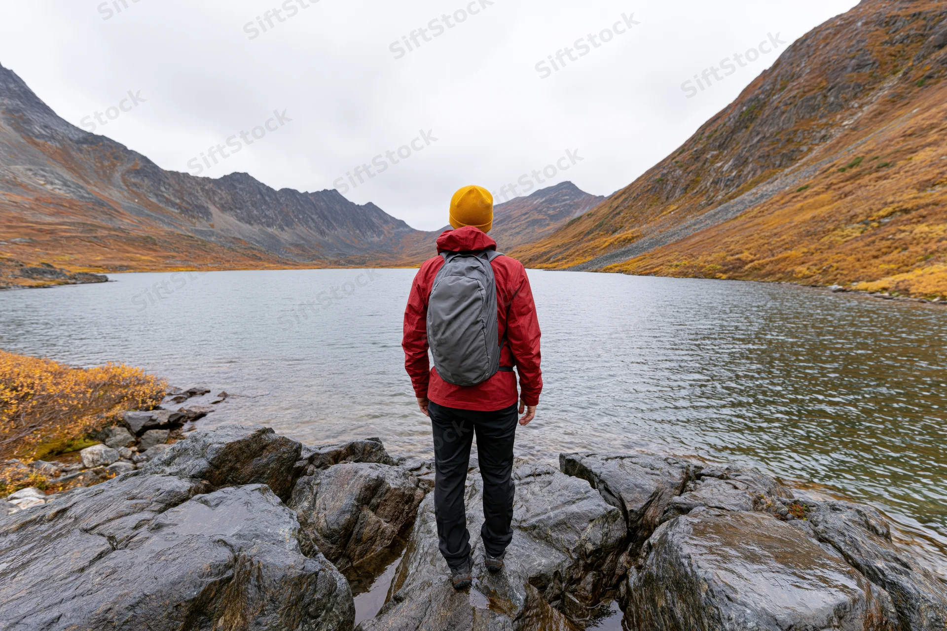 Hiker standing on rocky lakeshore facing mountains in autumn landscape