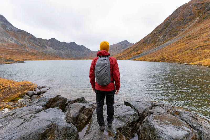 Hiker standing on rocky lakeshore facing mountains in autumn landscape