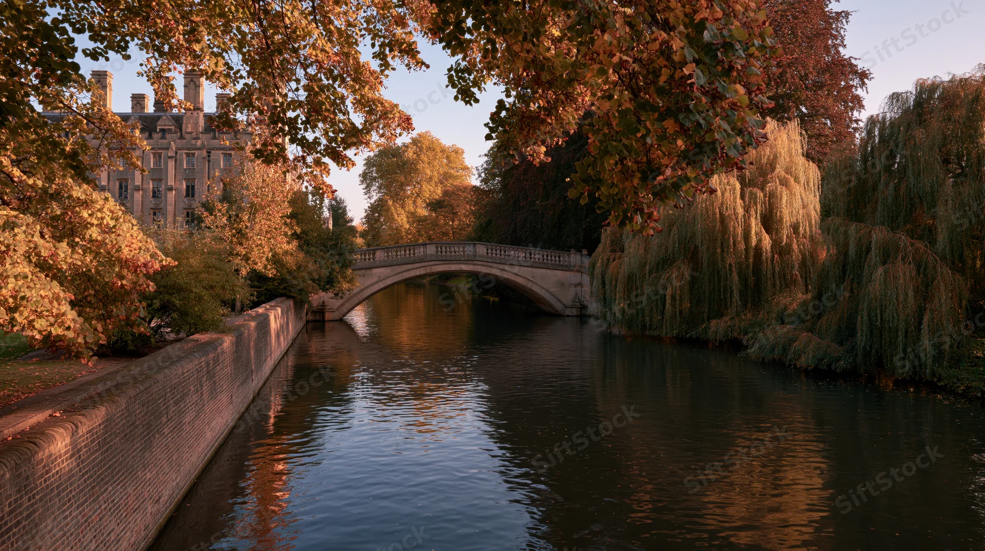 Stone arched bridge over calm river lined with autumn trees in cambridge